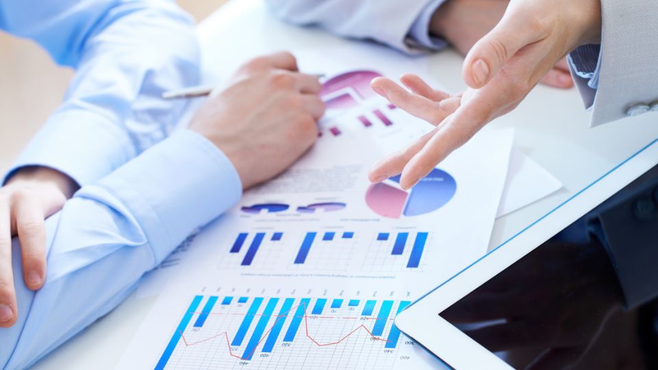 close up of two people's hands pointing at financial report documents